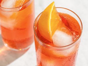 Two glasses of a cocktail garnished with orange wedges