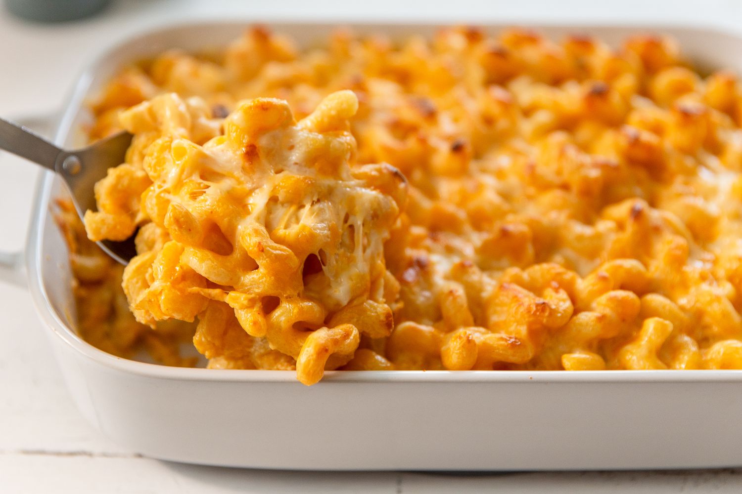 Side view of a white baking dish of macaroni and cheese with a serving spoon lifting a serving