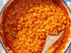 Cooked baked beans with a wooden spoon in a pot