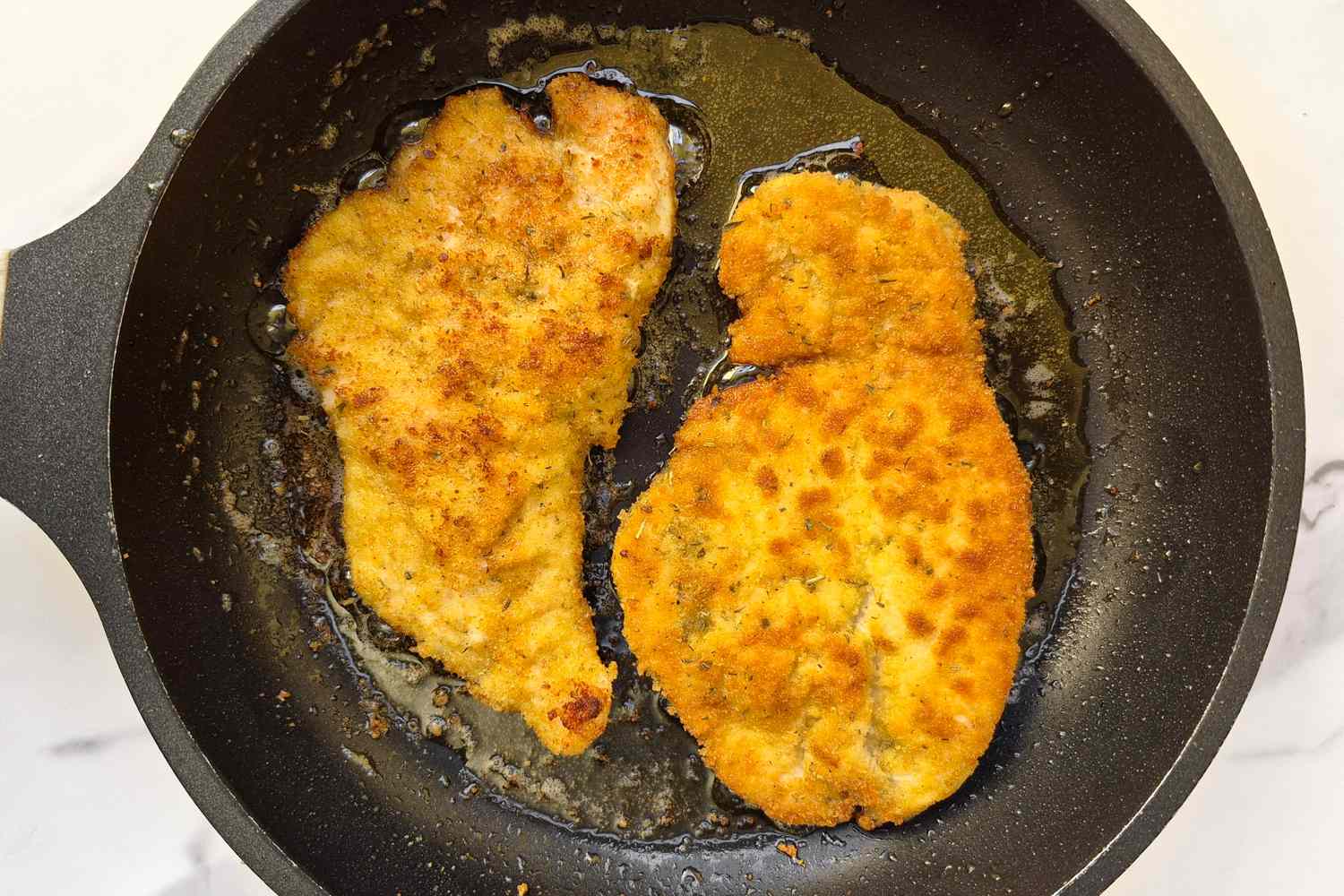 Two breaded chicken cutlets frying in a pan