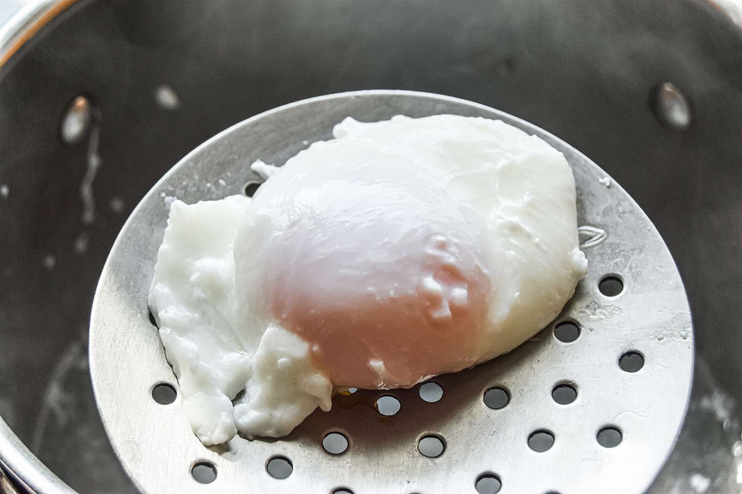 A poached egg resting on a slotted spoon