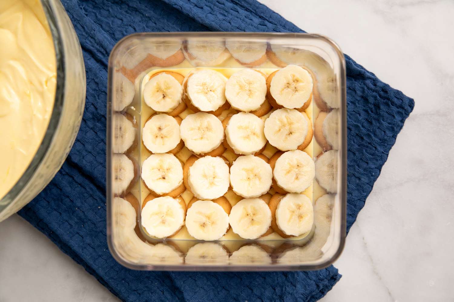 overhead view of banana slice layer on top of vanilla wafers layer on top of pudding layer in square dish for Southern Banana Pudding