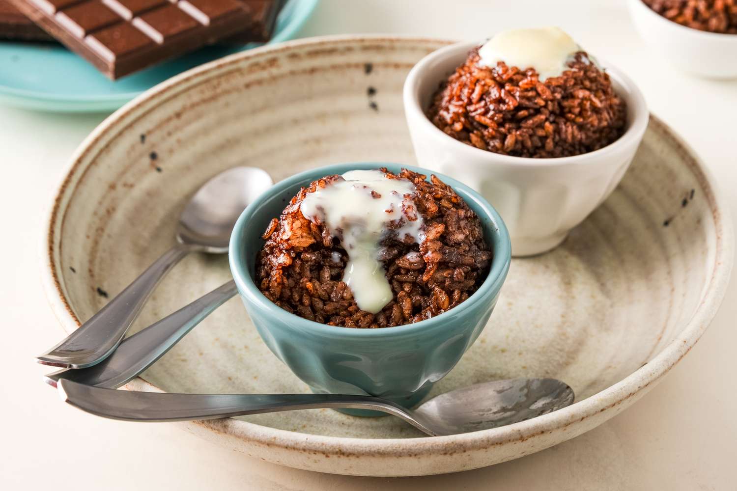 Bowls of chocolate rice dessert topped with cream on a large plate with spoons