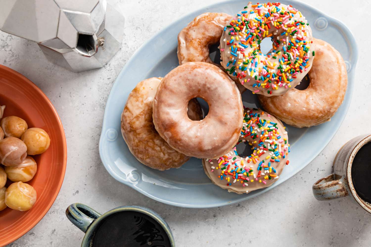 Platter of Glazed Donuts with Some Covered in Sprinkles, Next to Mugs of Coffee, a Moka, and Another Platter of Glazed Donut Wholes