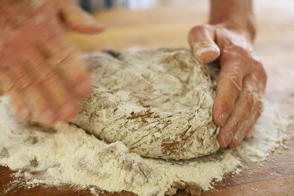 Hands kneading rye bread dough on a wooden table