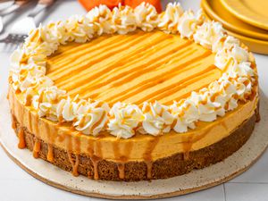 No-bake pumpkin cheesecake on a platter, and in the background, a stack of plates, utensils on the counter, and an orange kitchen towel