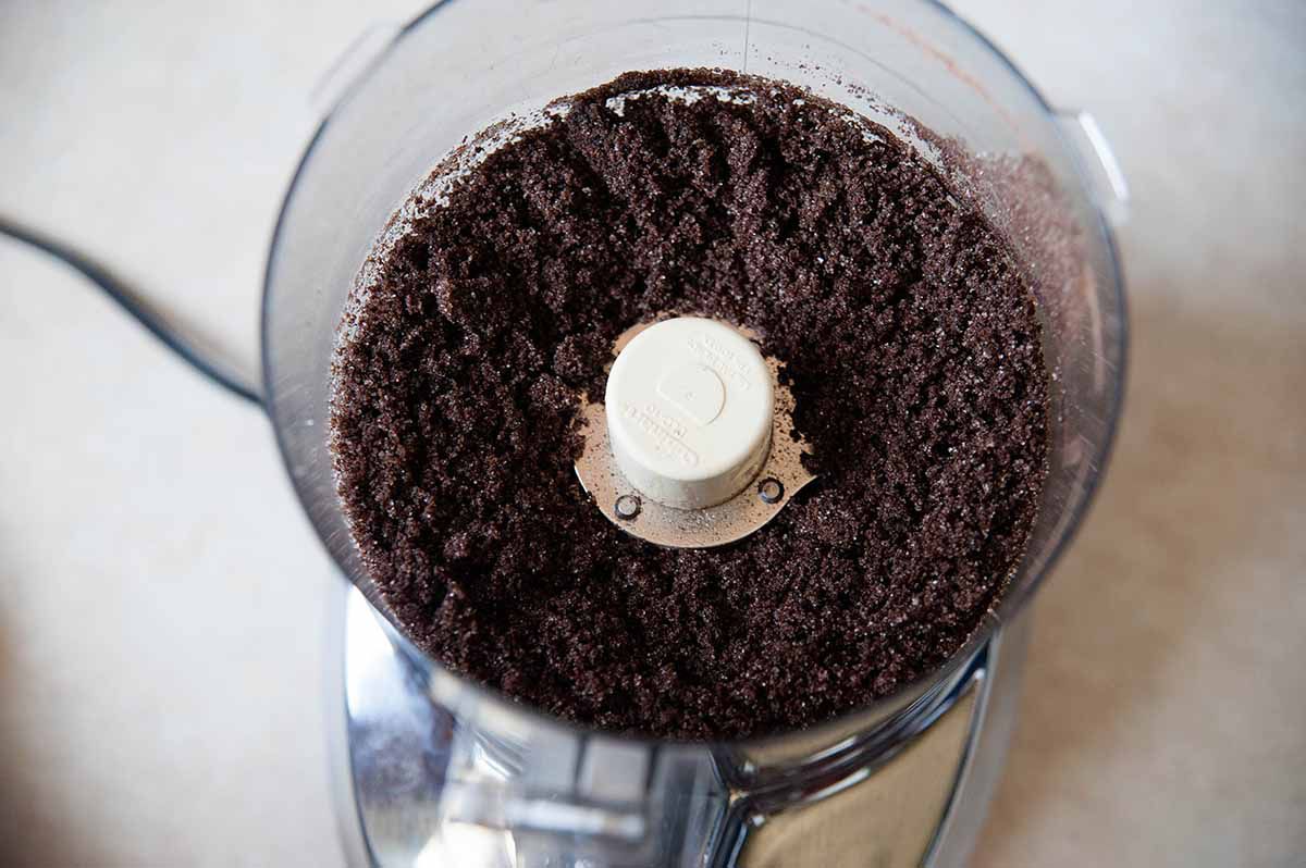 A shot of chocolate graham crackers ground up in a food processor with melted butter poured over the top to make the crust for a homemade chocolate cheesecake.