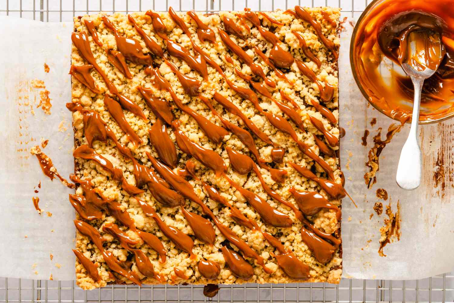 Caramel apple bars sliced and arranged on a parchment paperlined rack with extra caramel sauce in a bowl beside them