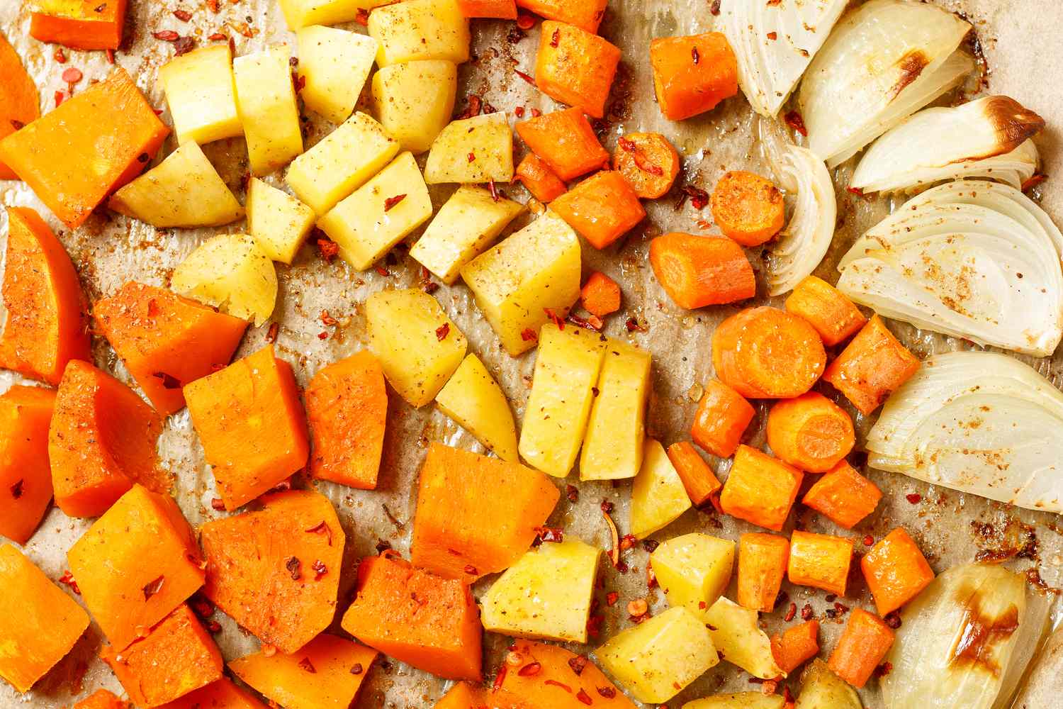 Assorted roasted vegetables including carrots sweet potatoes and onions on a baking sheet