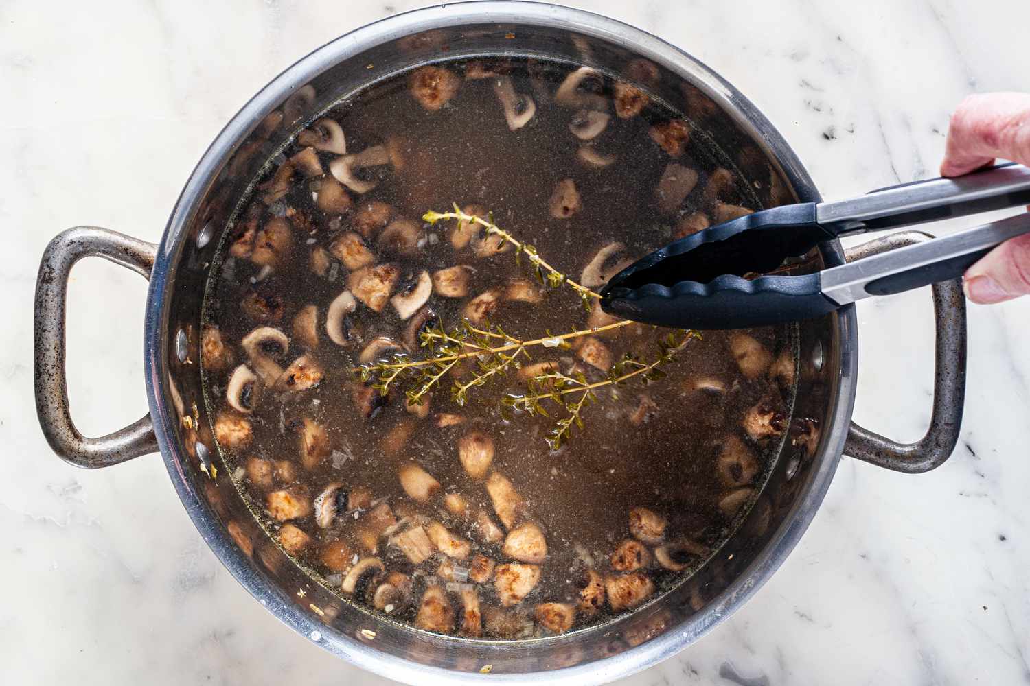 Tongs adding herbs to a pot of chestnut mushroom soup