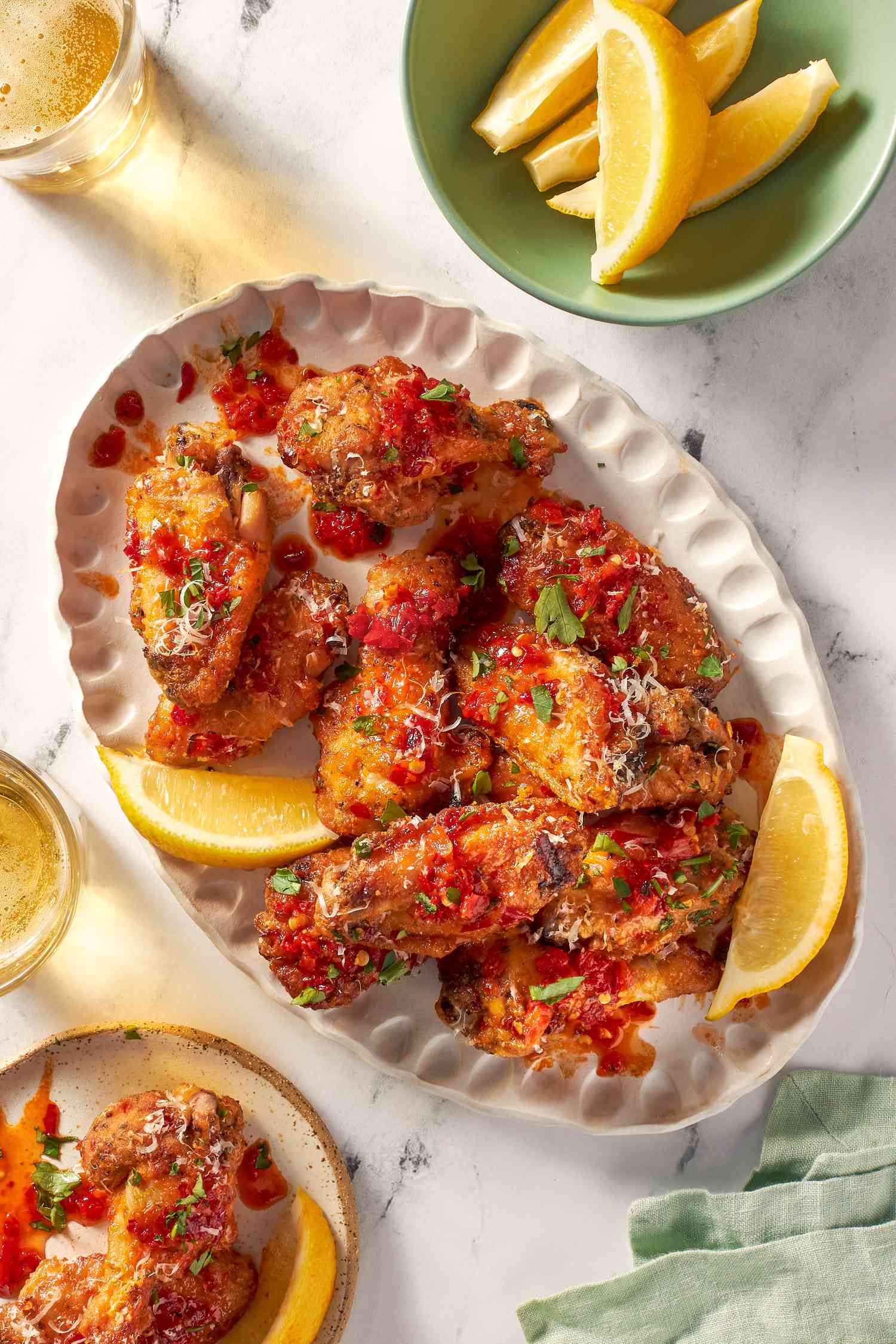 Chicken wings on a white platter with glasses of beer