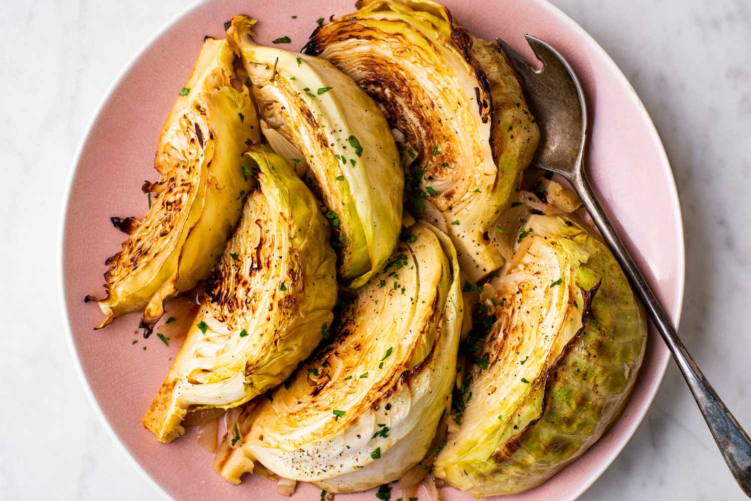 Overhead view of 6 wedges of melting cabbage on a pink plate with a serving spoon