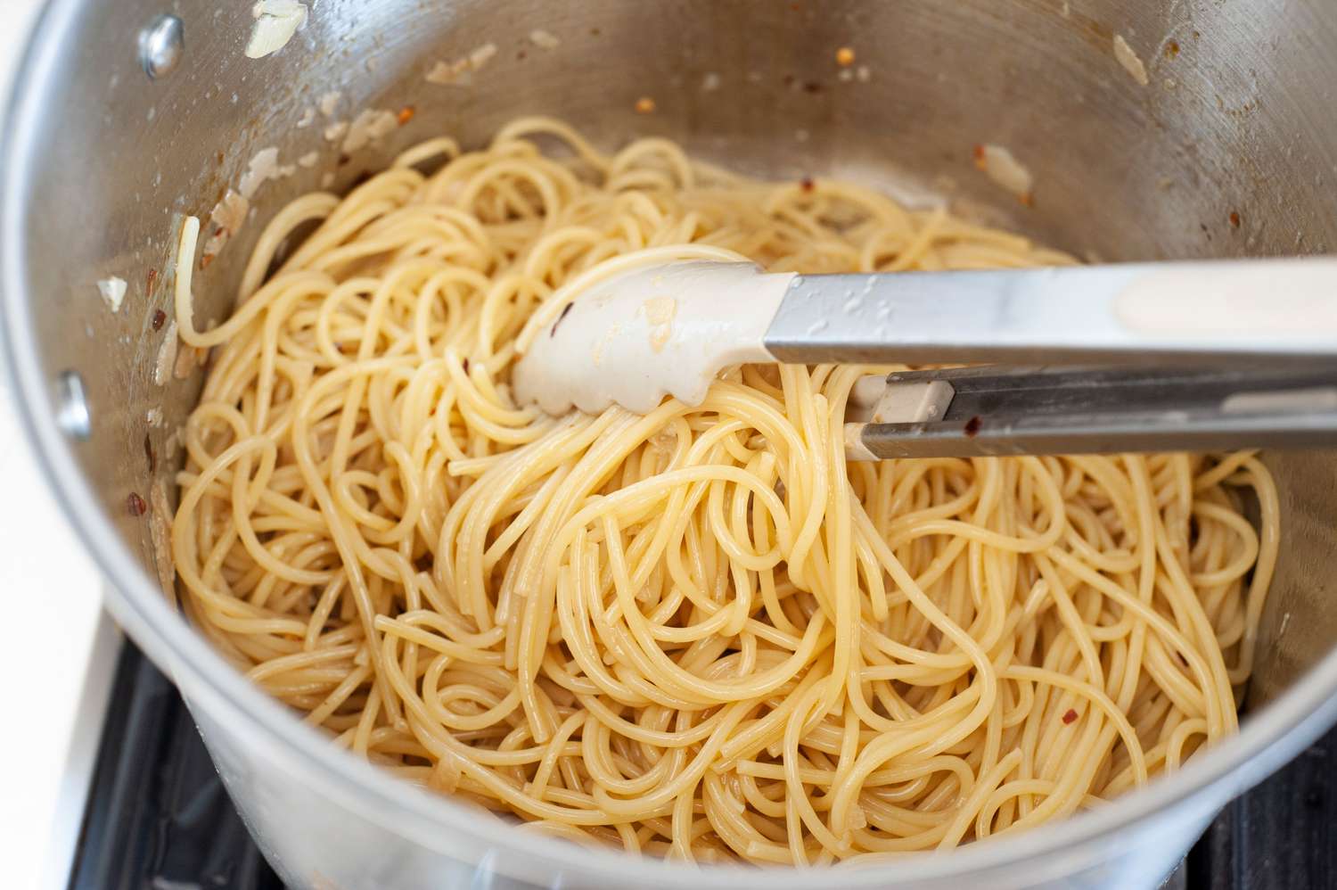Tongs Stirring Spaghetti Aglio e Olio in Pot
