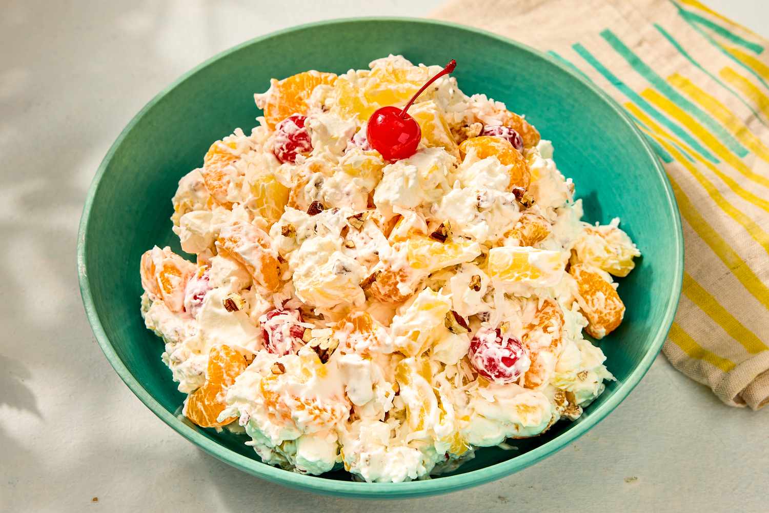 A bowl of ambrosia salad with fruit and a cherry on top