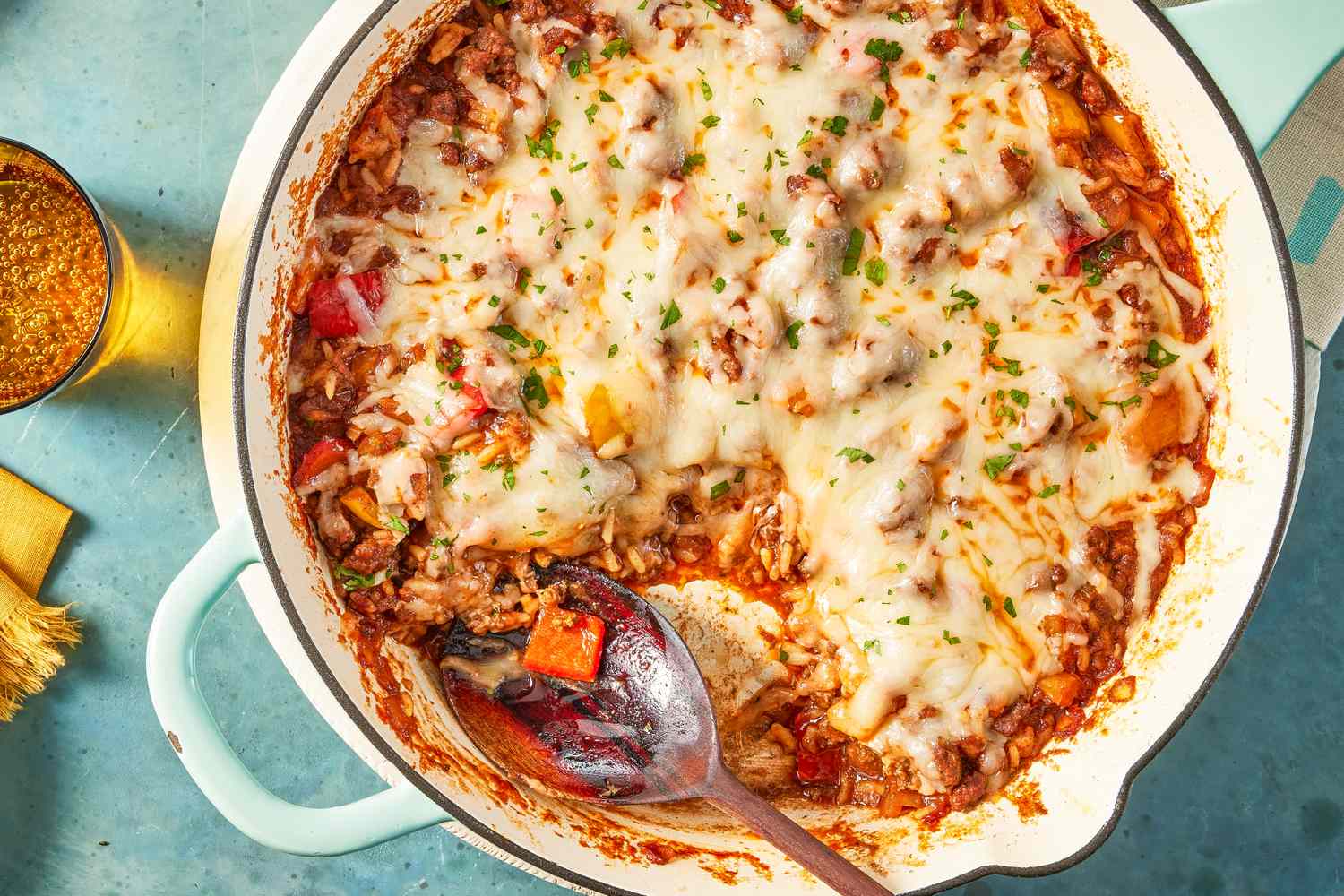 unstuffed peppers in a skillet at a table setting with glasses of water, paper towels, and a small bowl of minced herbs