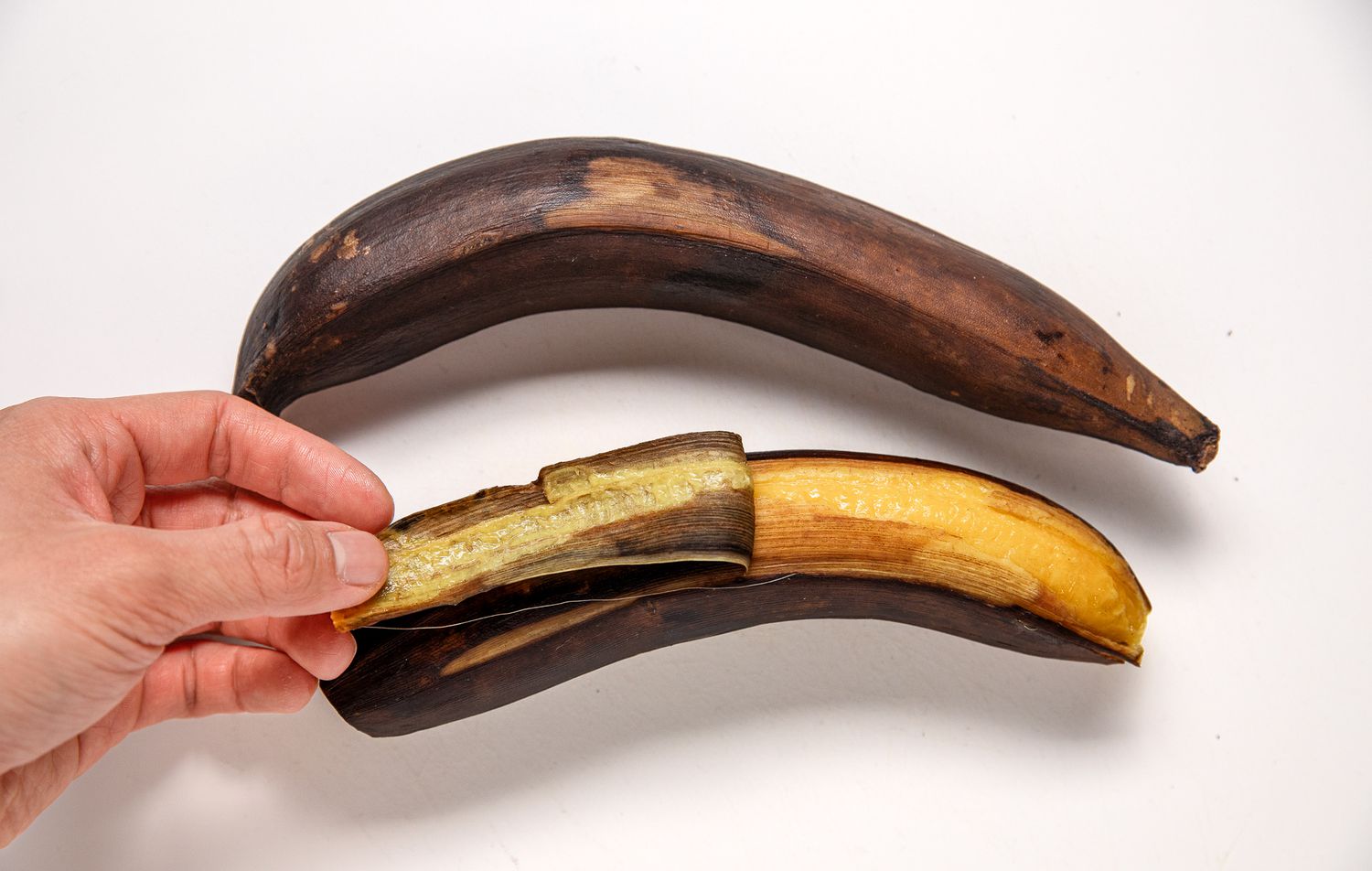 Hand Removing the Peel From a Ripened Plantain and a Plantain With the Peel Still Intact