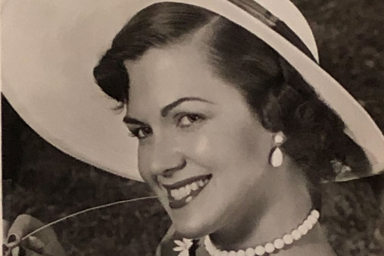 A smiling woman wearing a hat and jewelry