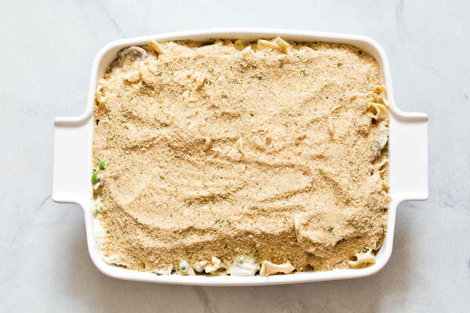 Overhead view of a white baking dish of un-baked Chicken Tetrazzini Casserole recipe after adding the breadcrumbs and Parmesan cheese topping
