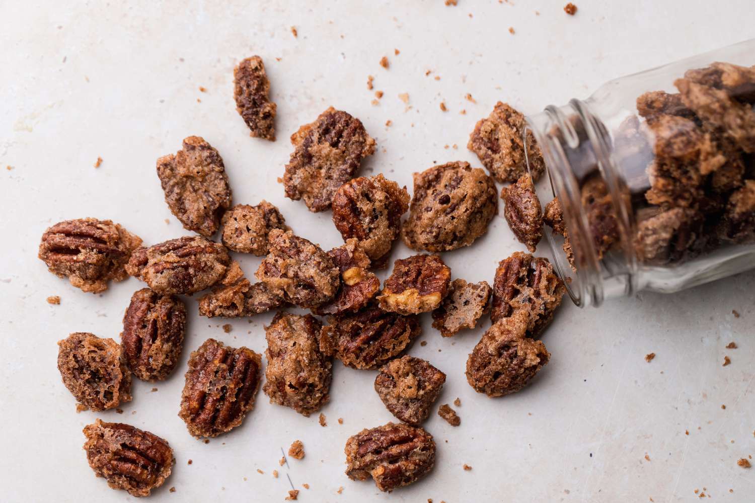 A glass jar tipped over with sugared pecans spilling out from it.