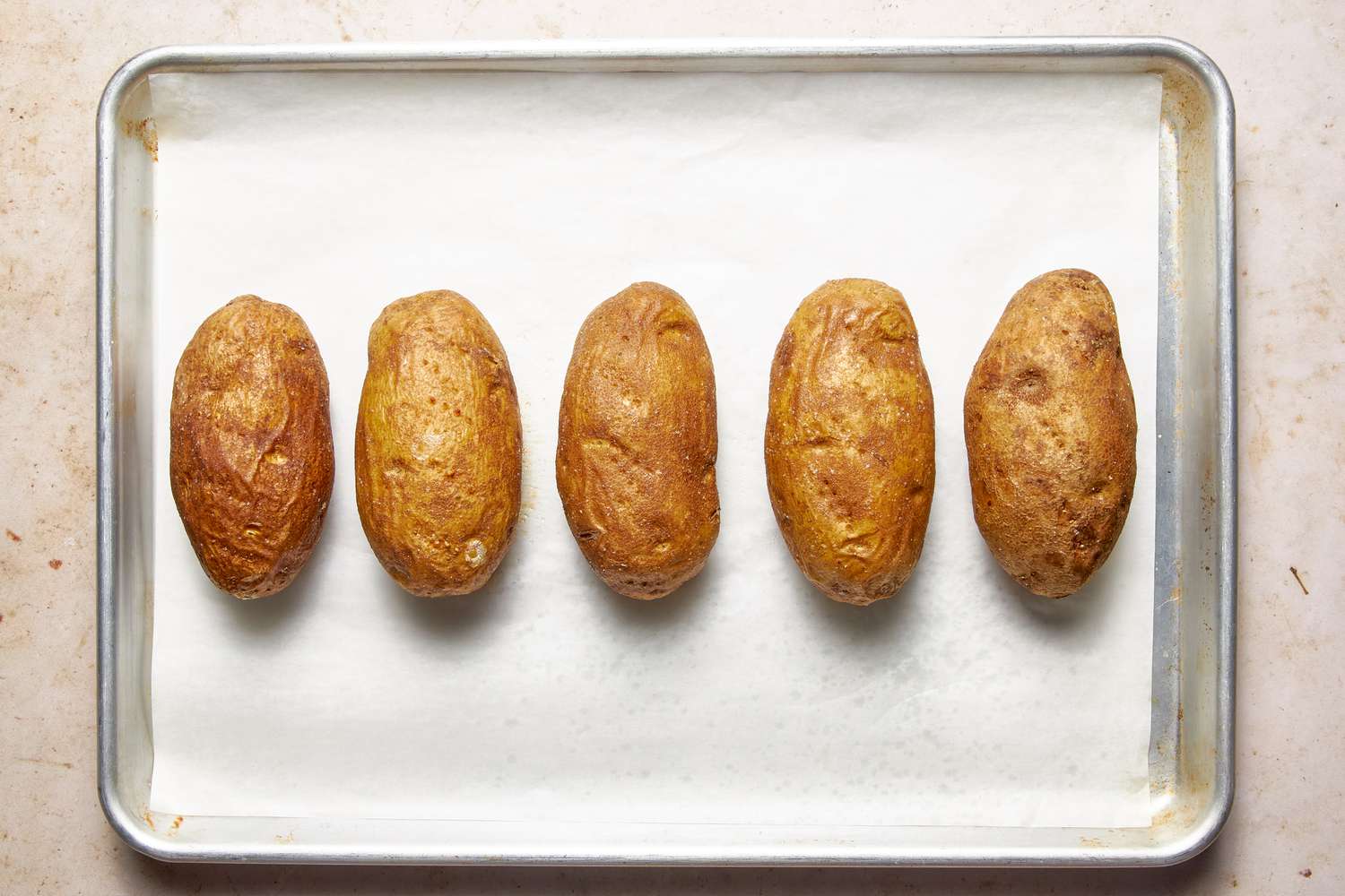 Whole baked potatoes on a parchment paper-lined baking tray for twice baked potatoes recipe