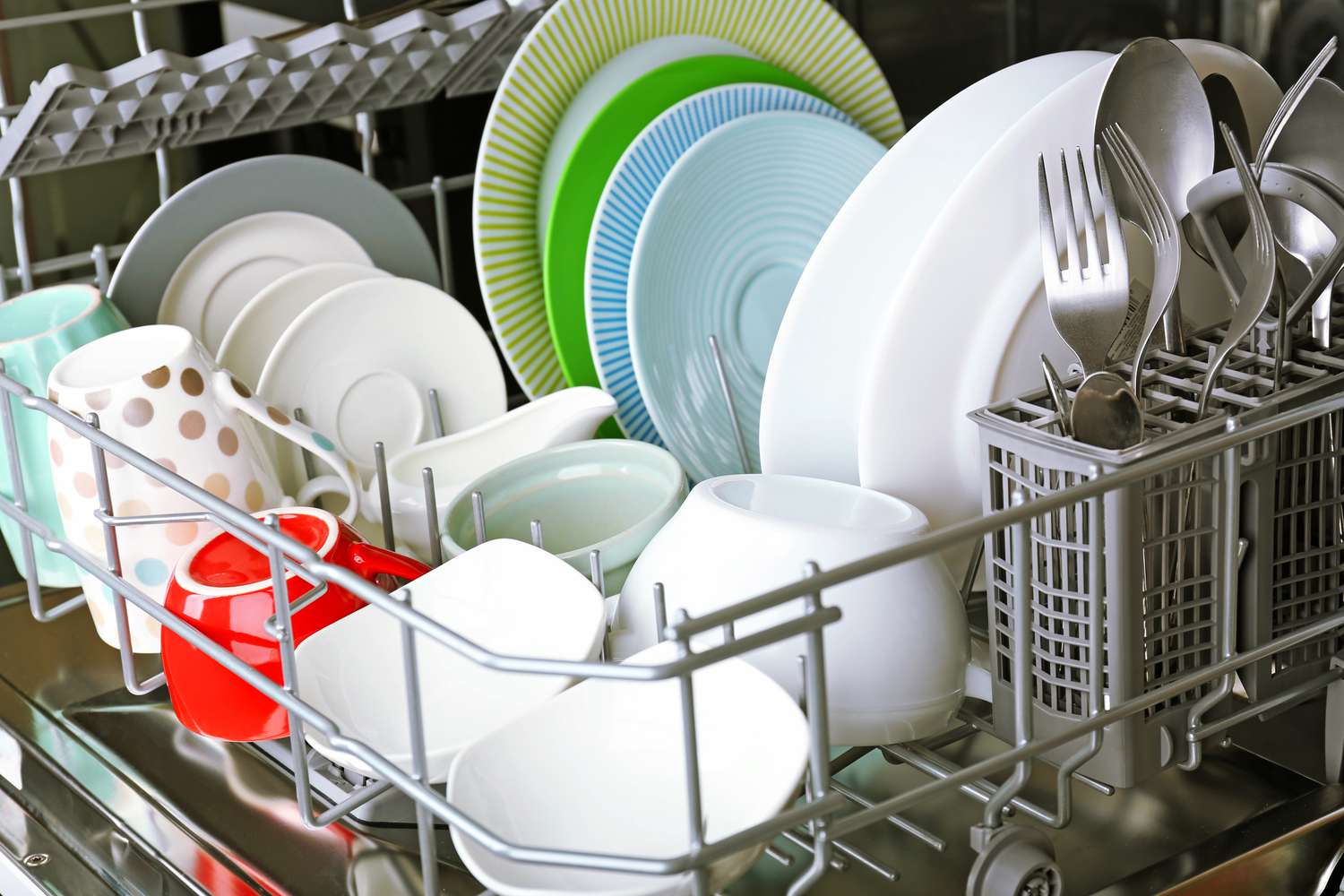 Open dishwasher with loaded plates, bowls, cups, and cutlery