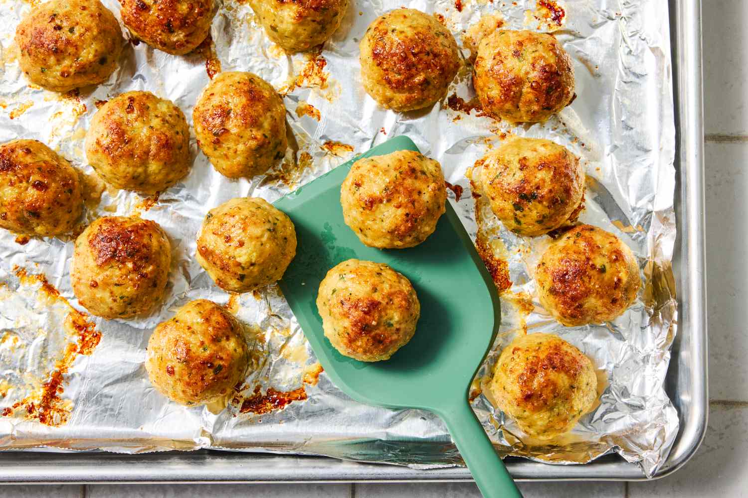 Baked chicken meatballs on a foillined tray with some on a spatula