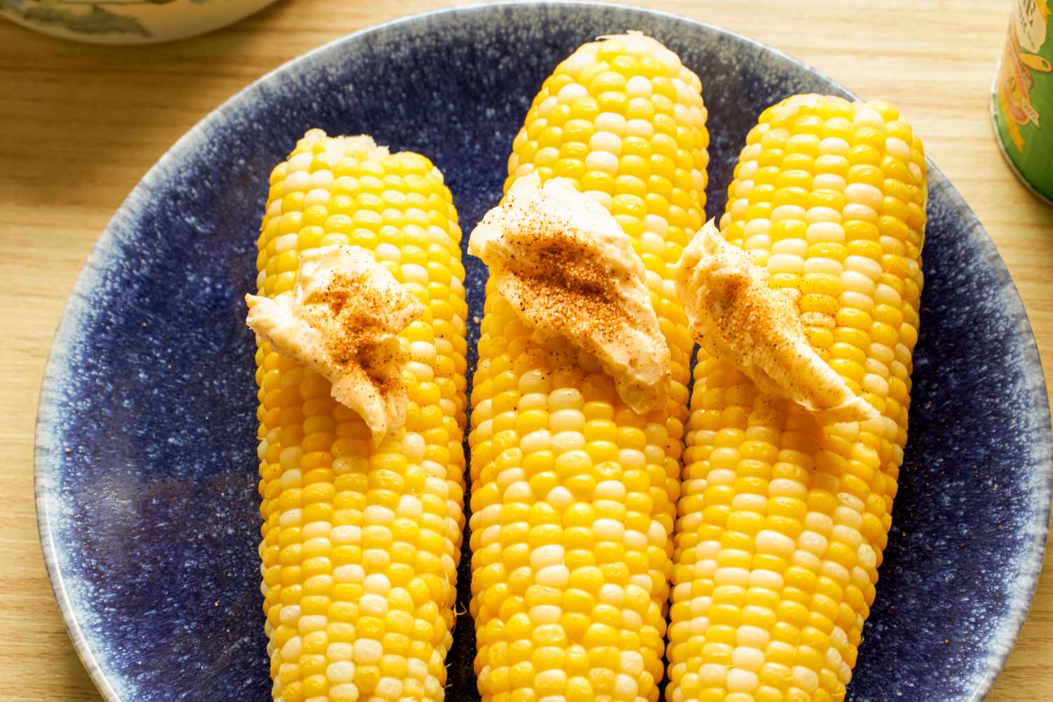 Three corn on the cobs on a plate topped with butter and spices