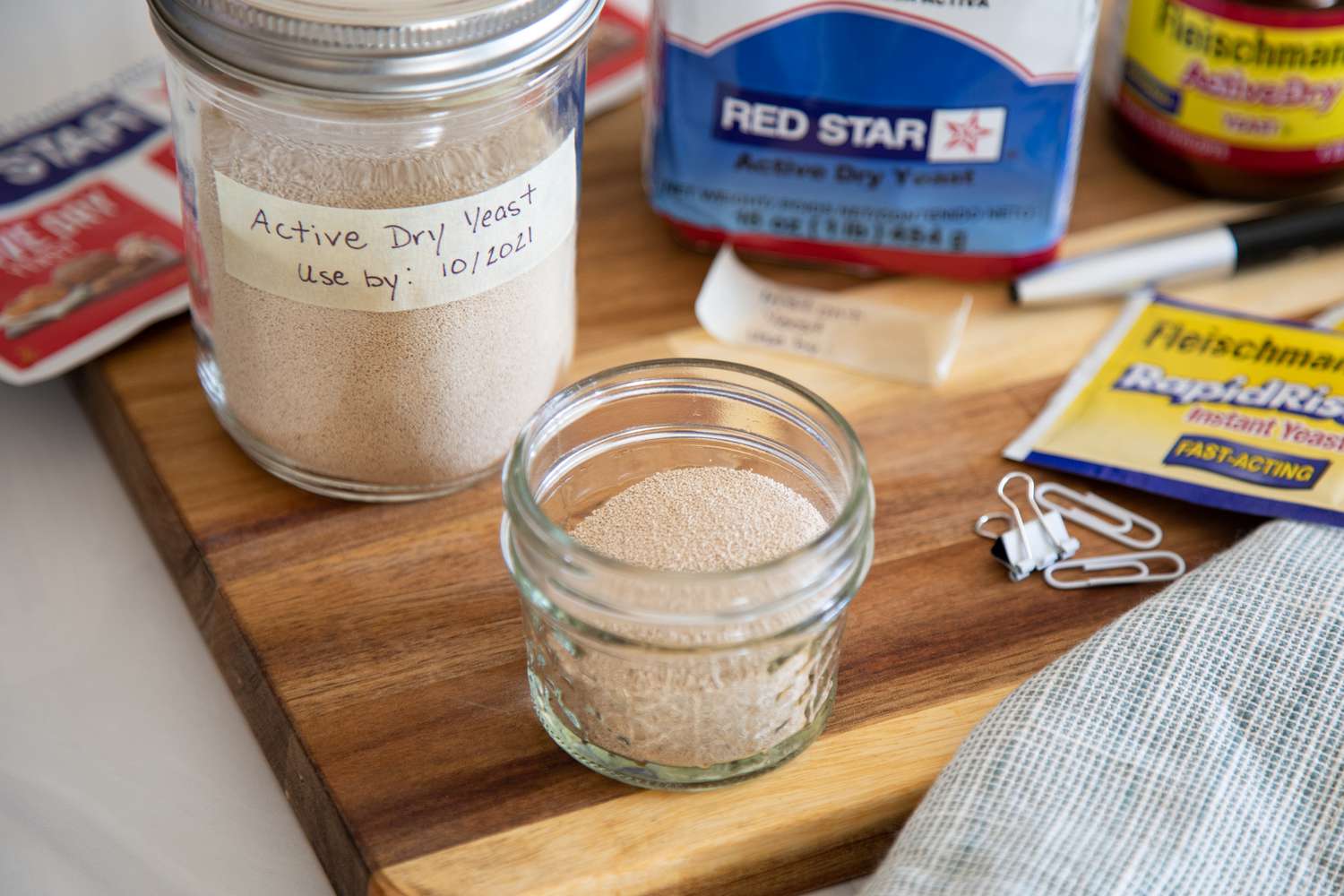 A wooden cutting board with a variety of yeast in their packaging and in mason jars to show how to store yeast.