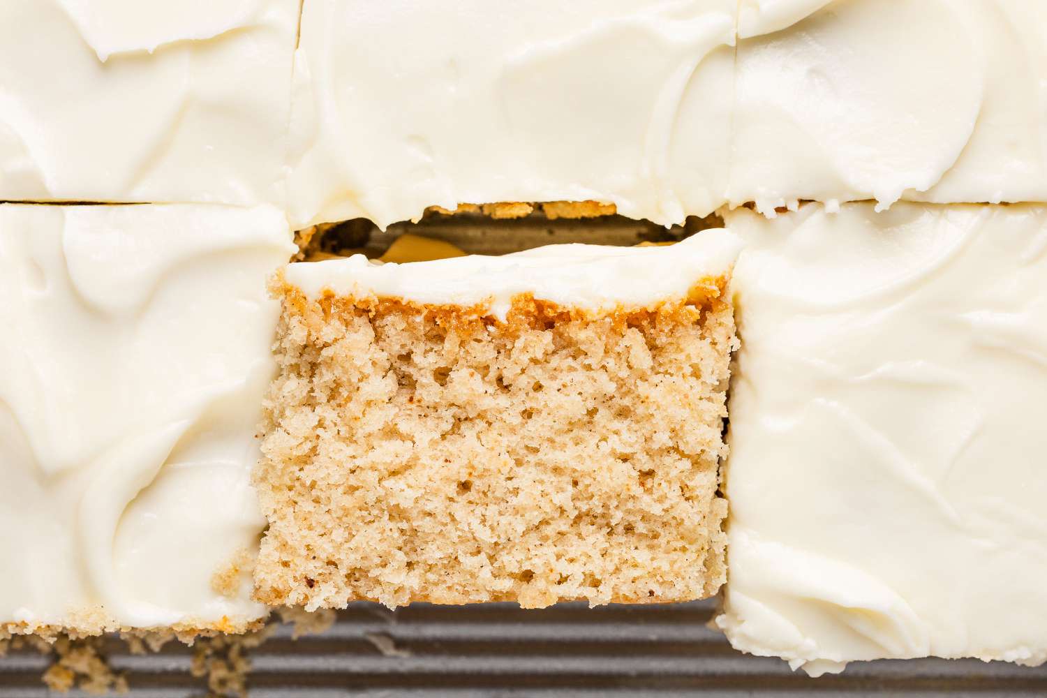view from above of iced, cut cake in a square tin, close up, with one slice of cake turned over to reveal the crumb of the Feather Cake