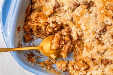 A closeup of a blue baking dish with apple dump cake, with one part of the cake having been scooped out, and a golden spoon placed in the dish for serving the cake
