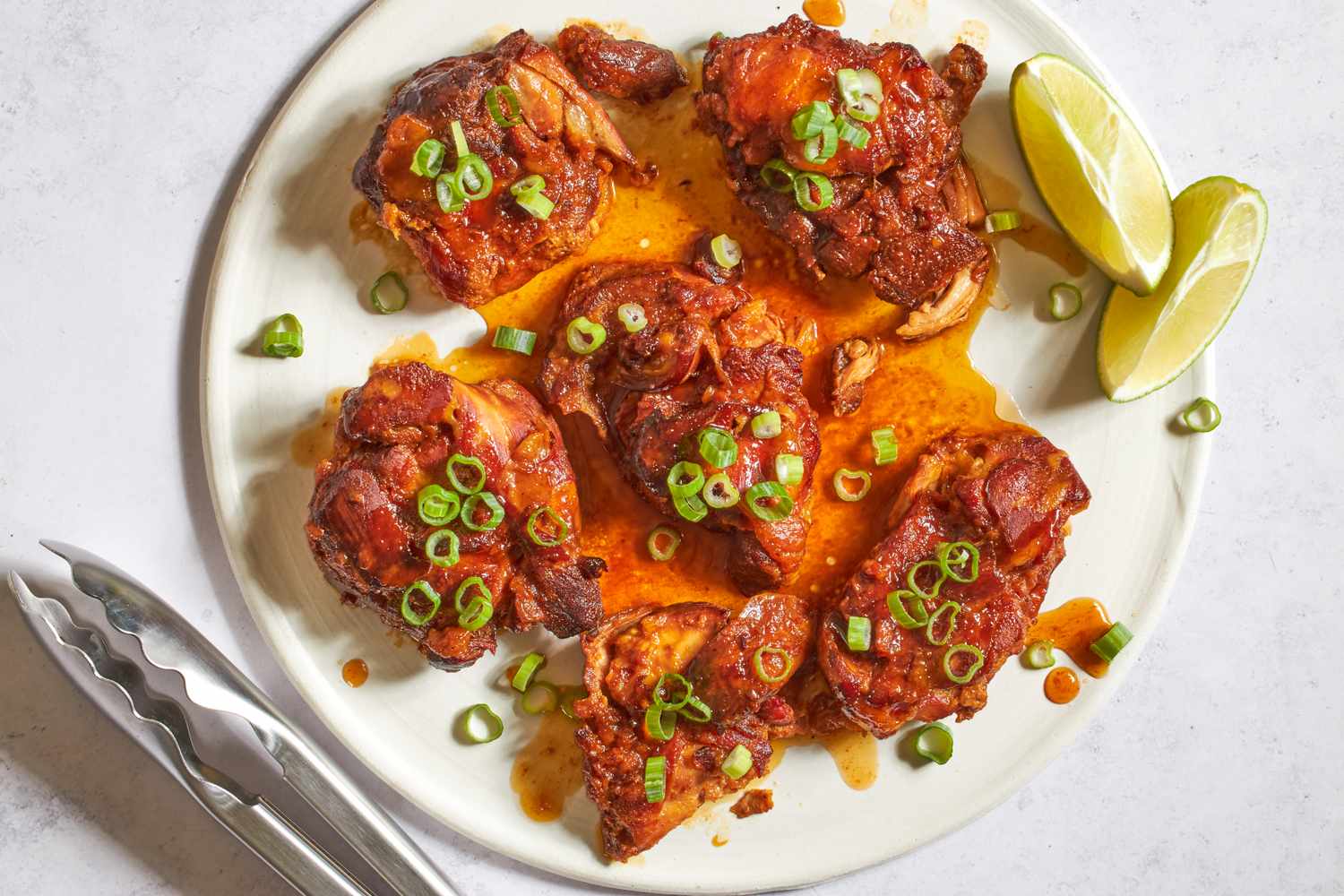Plate of hot honeyglazed chicken thighs with green onion garnish and lime wedges