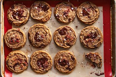 Freshly baked cookies on a baking sheet with a nonstick liner topped with chocolate chunks and flaky salt