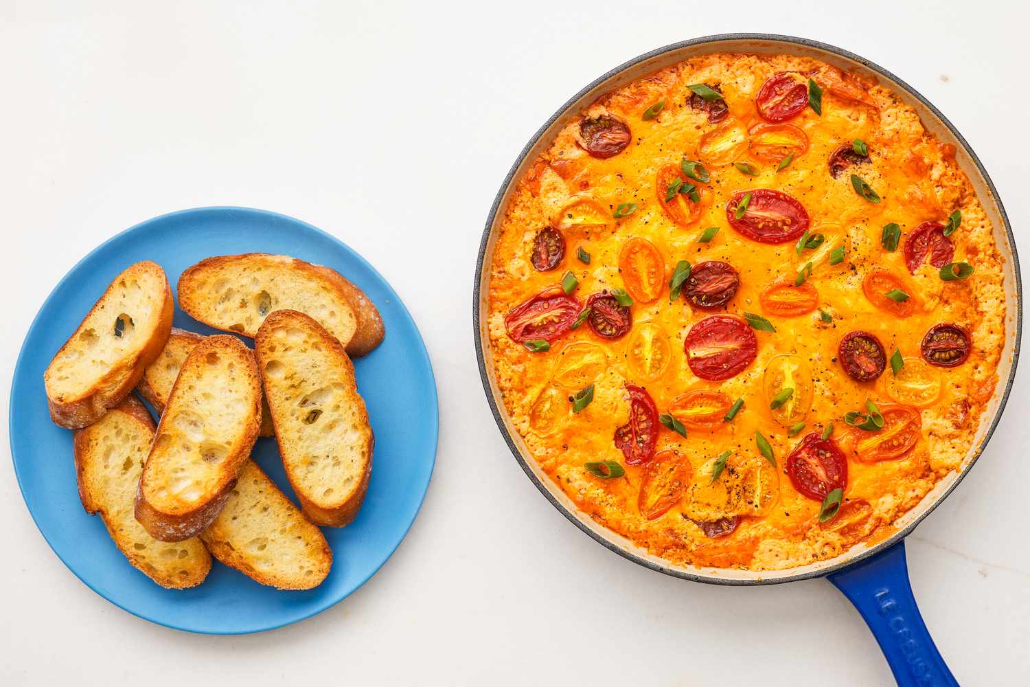 tomato pie dip in a pan next to a plate with toasted baguette slices 