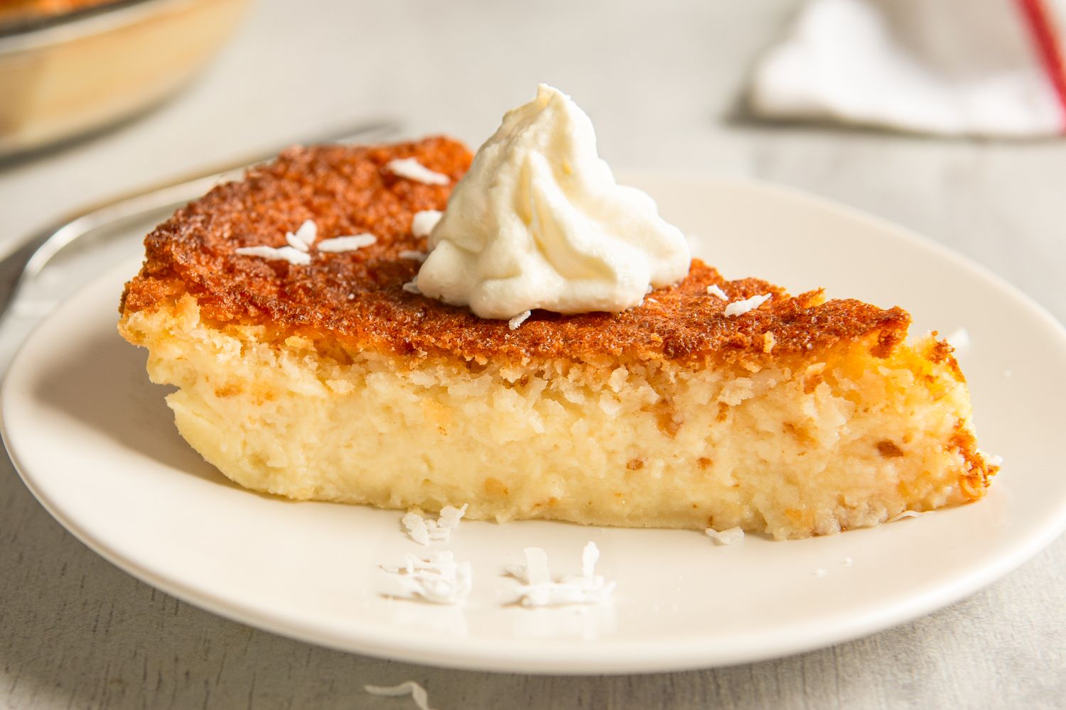 A slice of pie topped with whipped cream on a plate showing a golden crust and a moist interior