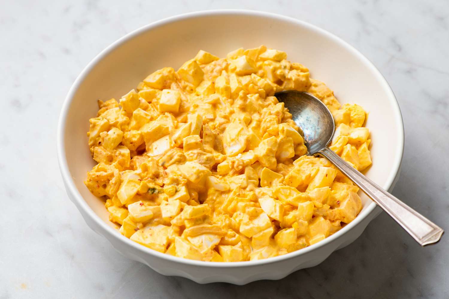 A bowl with kimchi egg salad and a spoon