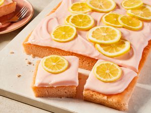 pink lemonade cake (with some slices cut out) on a board next to a plate with a slice 