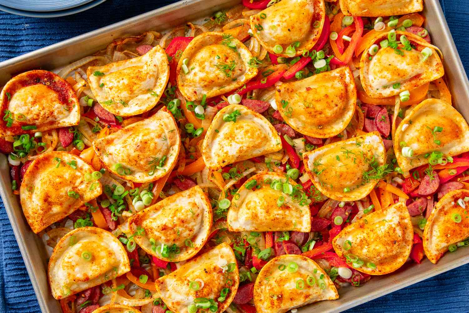 A tray of baked pierogis garnished with green onions layered over sauted vegetables