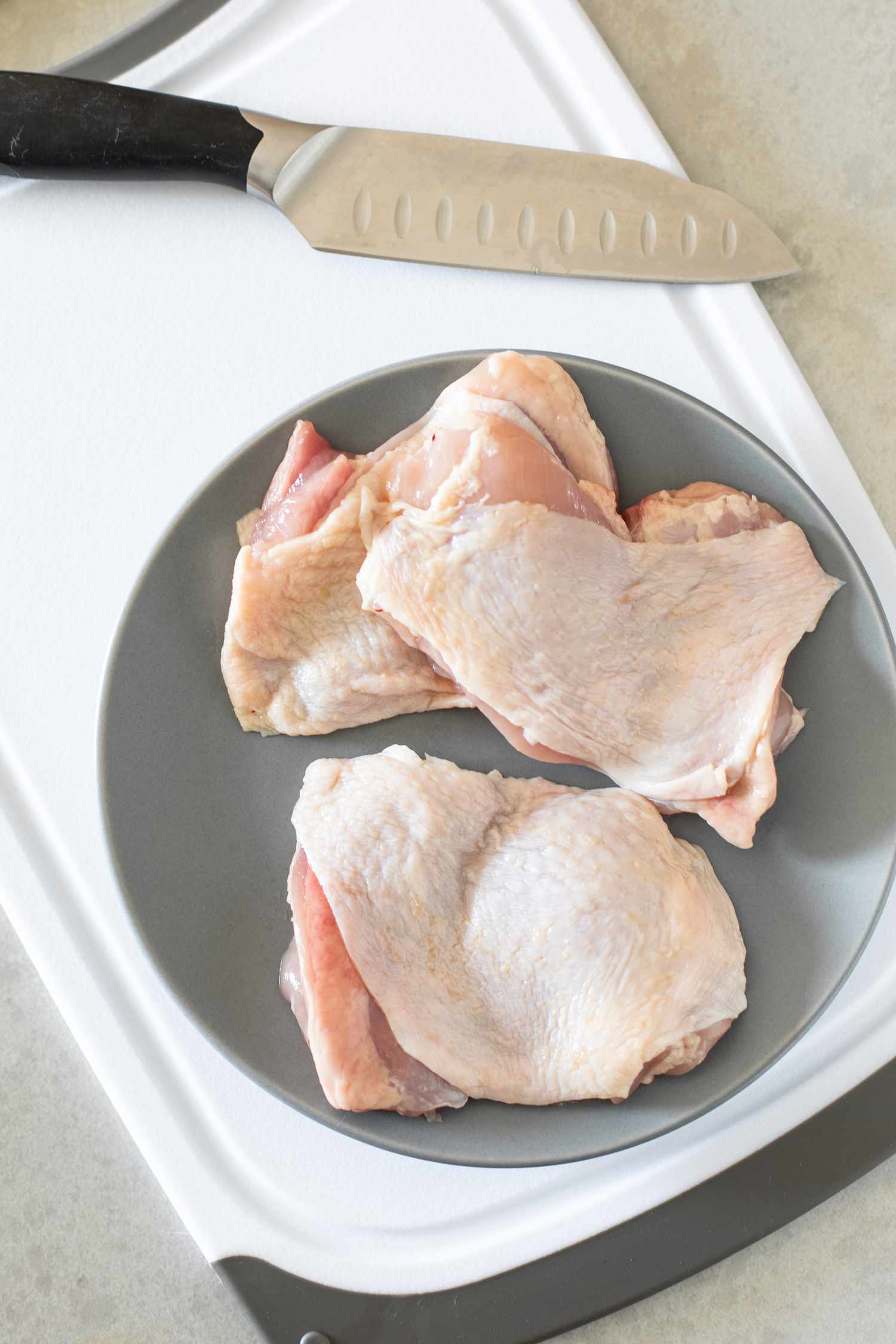 Plate of Boneless Chicken Thighs Next to a Knife on a Cutting Board 