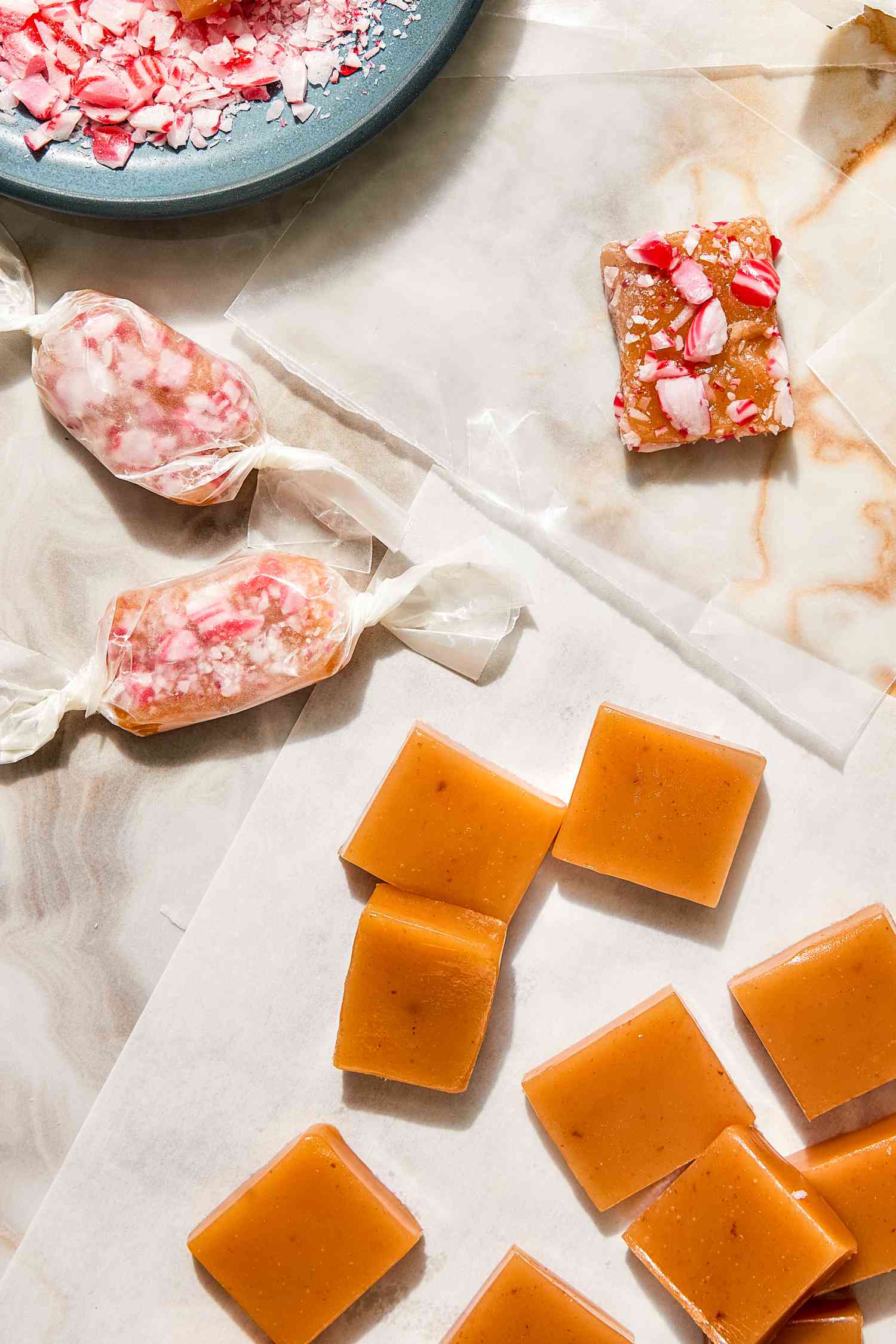 Peppermint Caramels with Some Wrapped in Wax Paper, Some Topped with Crushed Candy Cane, and Some Without Toppings, All Next to a Small Bowl of Crushed Candy Canes