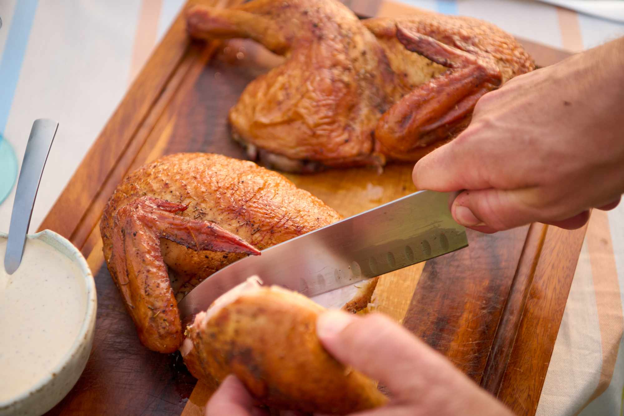 A person slicing roast chicken on a wooden cutting board during meal preparation