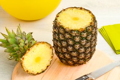 Pineapple with top removed showing interior flesh on a wooden cutting board with a knife nearby