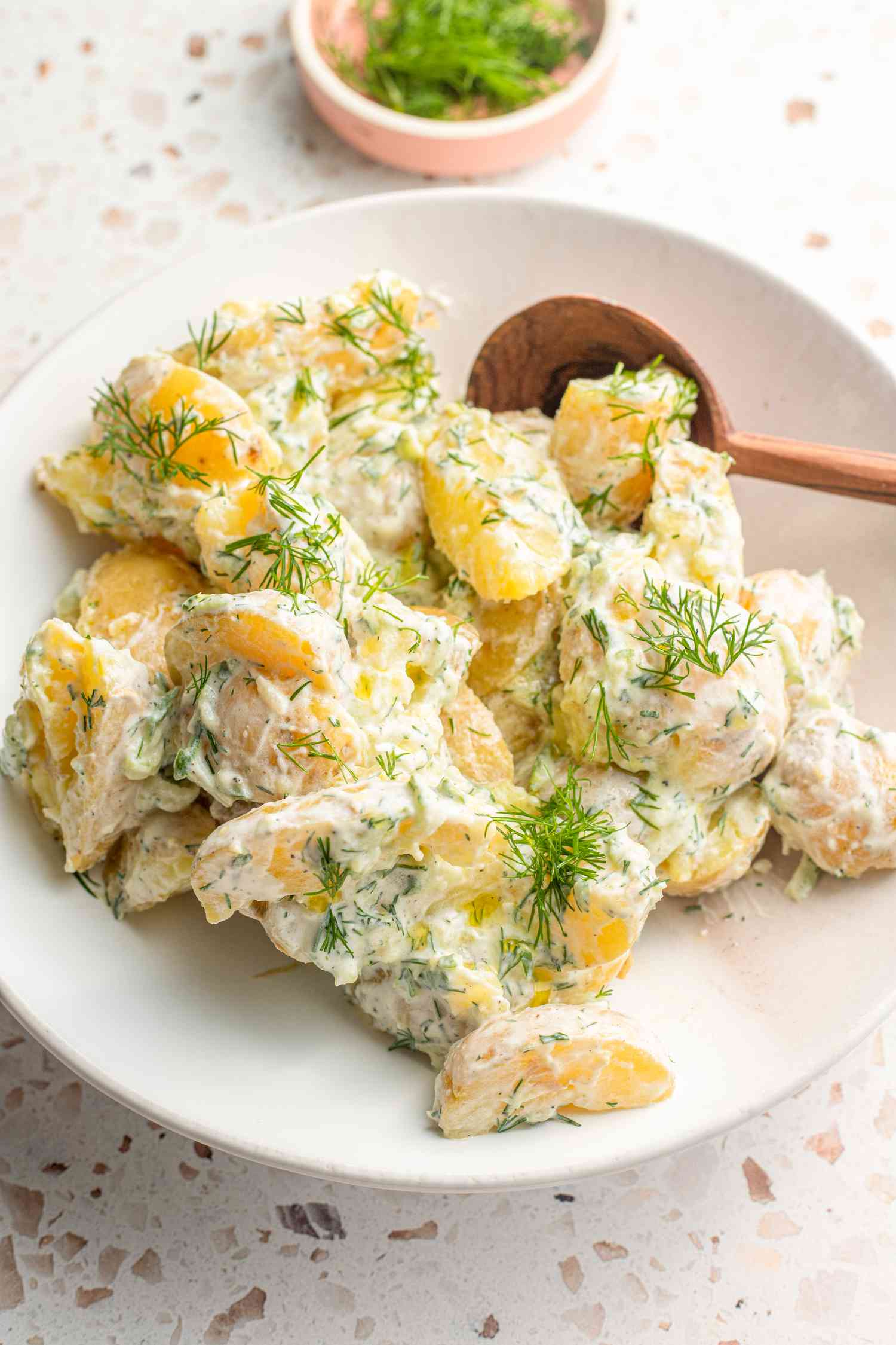 tzatziki potato salad in a bowl with a serving spoon, and in the background, a bowl of dill 