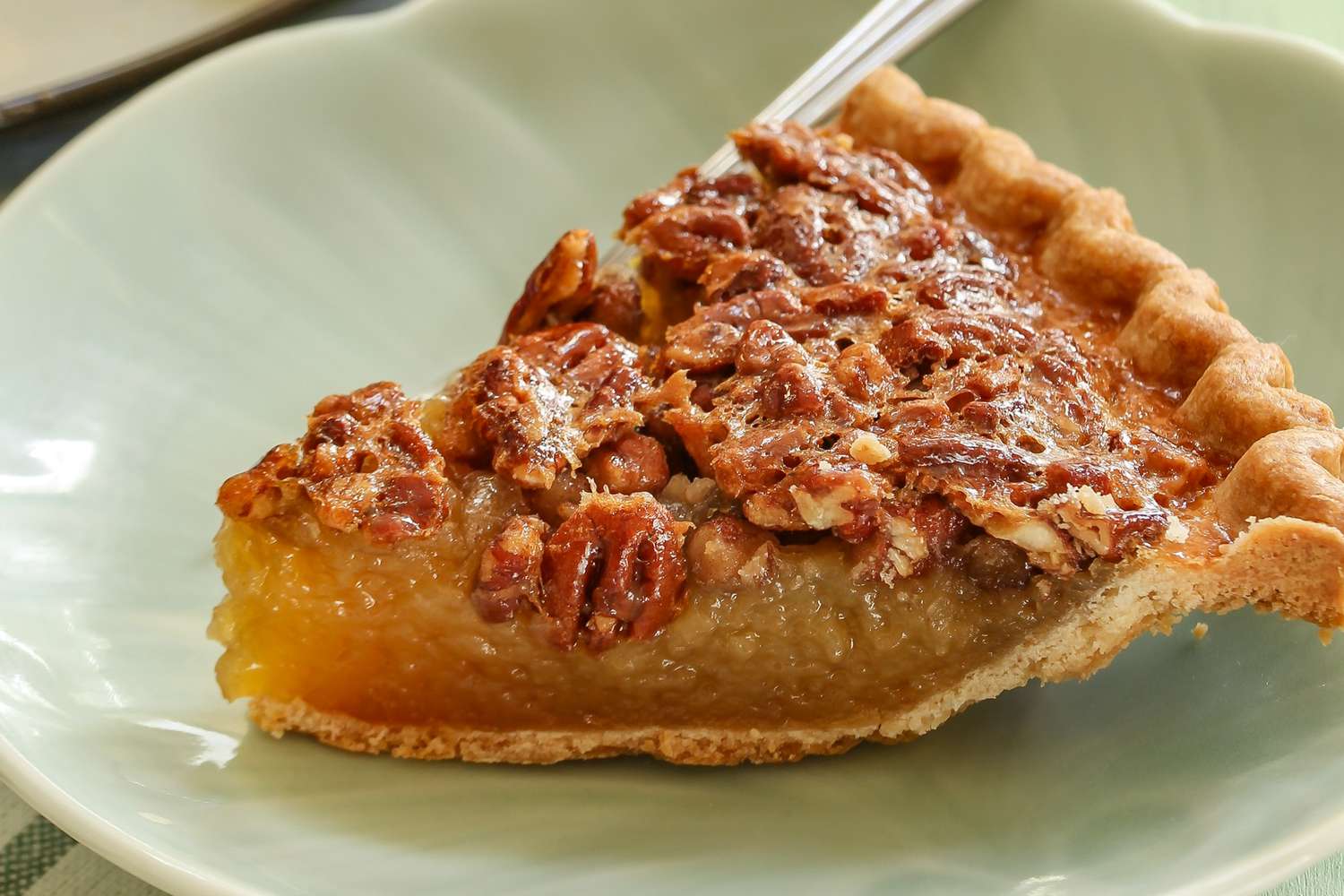 Closeup view of a slice of pecan pie on a light green plate along with a fork