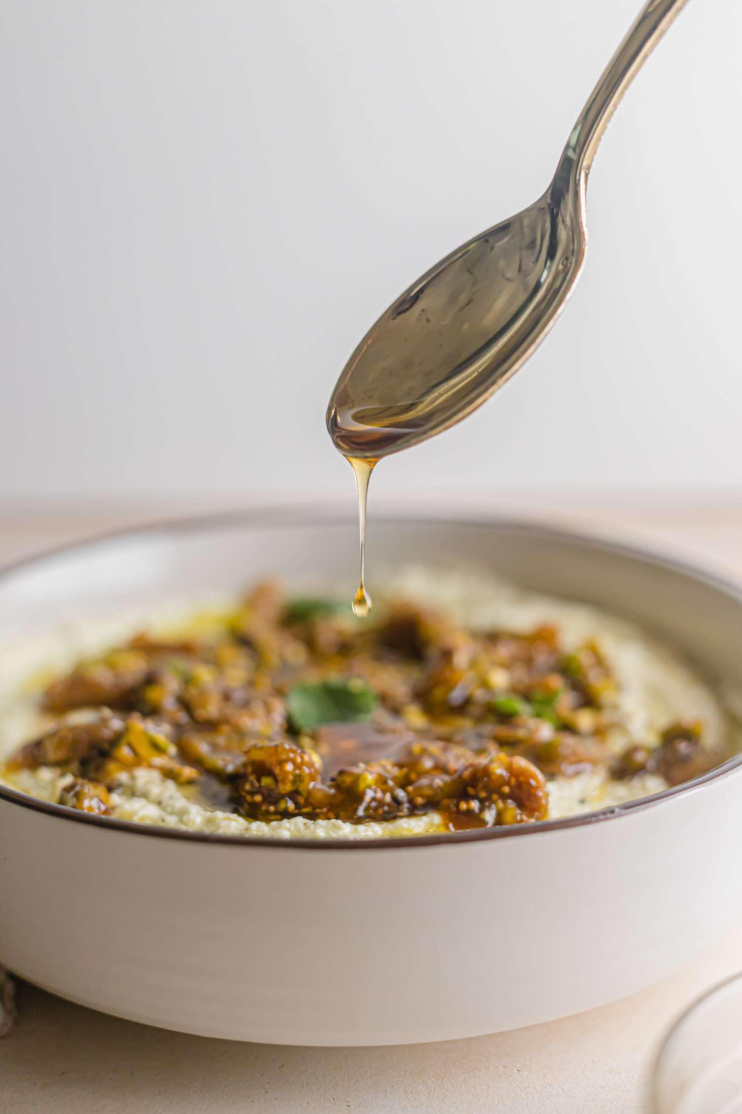 Spooning honey over a bowl of whipped feta with figs, pistachios, and a honey drizzle.