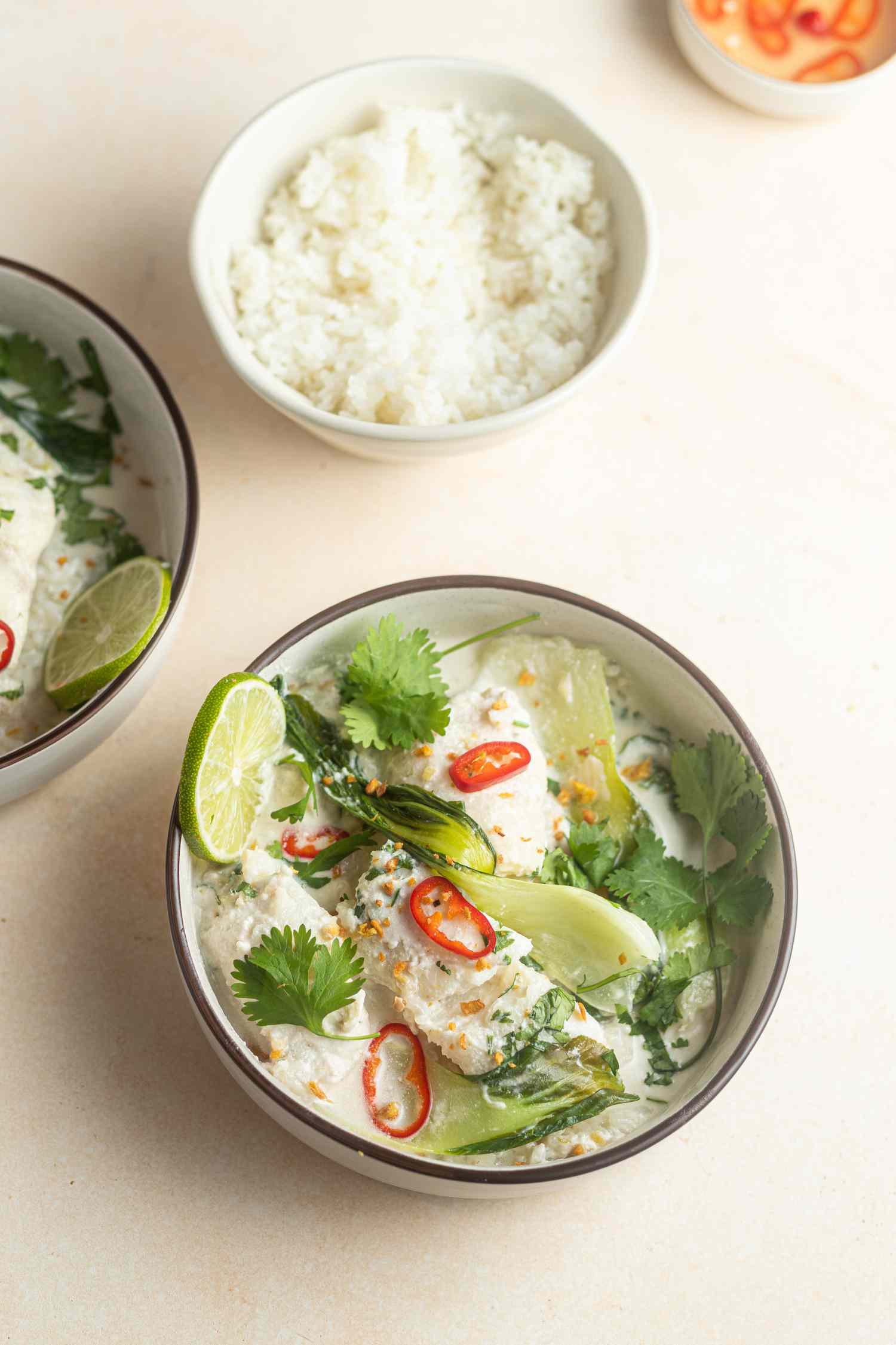Overhead view of two bowls of Coconut poached cod with ginger and lime served with lime and rice.