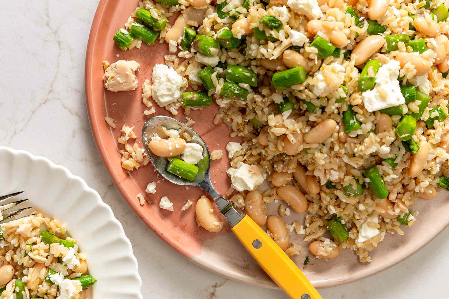 Dish of asparagus and brown rice with white beans and cheese crumbles on a plate, served with a spoon