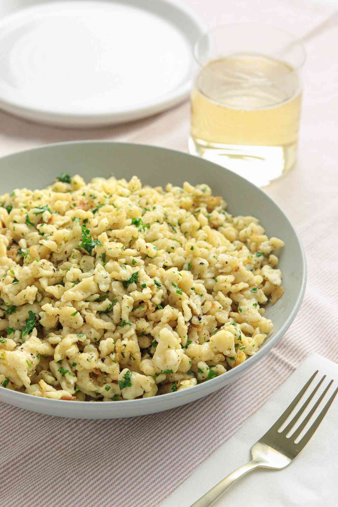 Bowl of Homemade Spaetzle (Spätzle) at a Table Setting with a Drink and a Fork on a Table Napkin