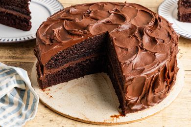 black magic cake on a platter with a slice cut out and in the background, two plates with some cake slices