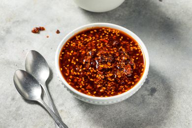 A bowl of chili crisp beside two spoons on a gray surface