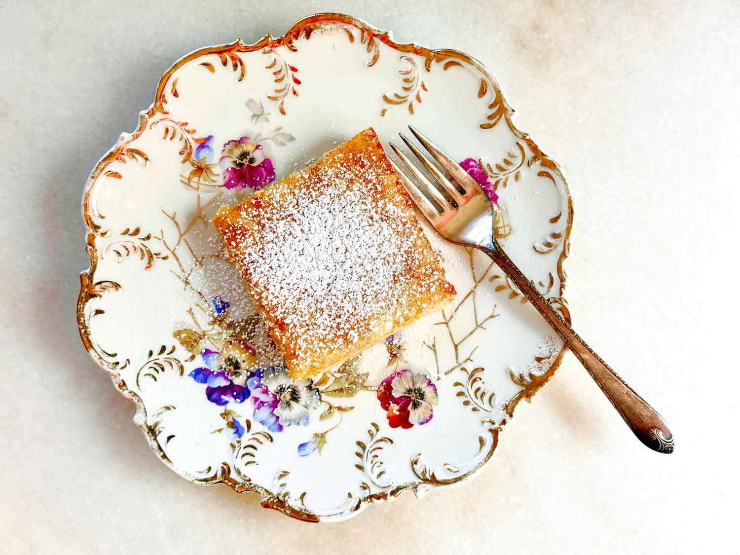 A lemon square served on a decorative plate with a fork on the side